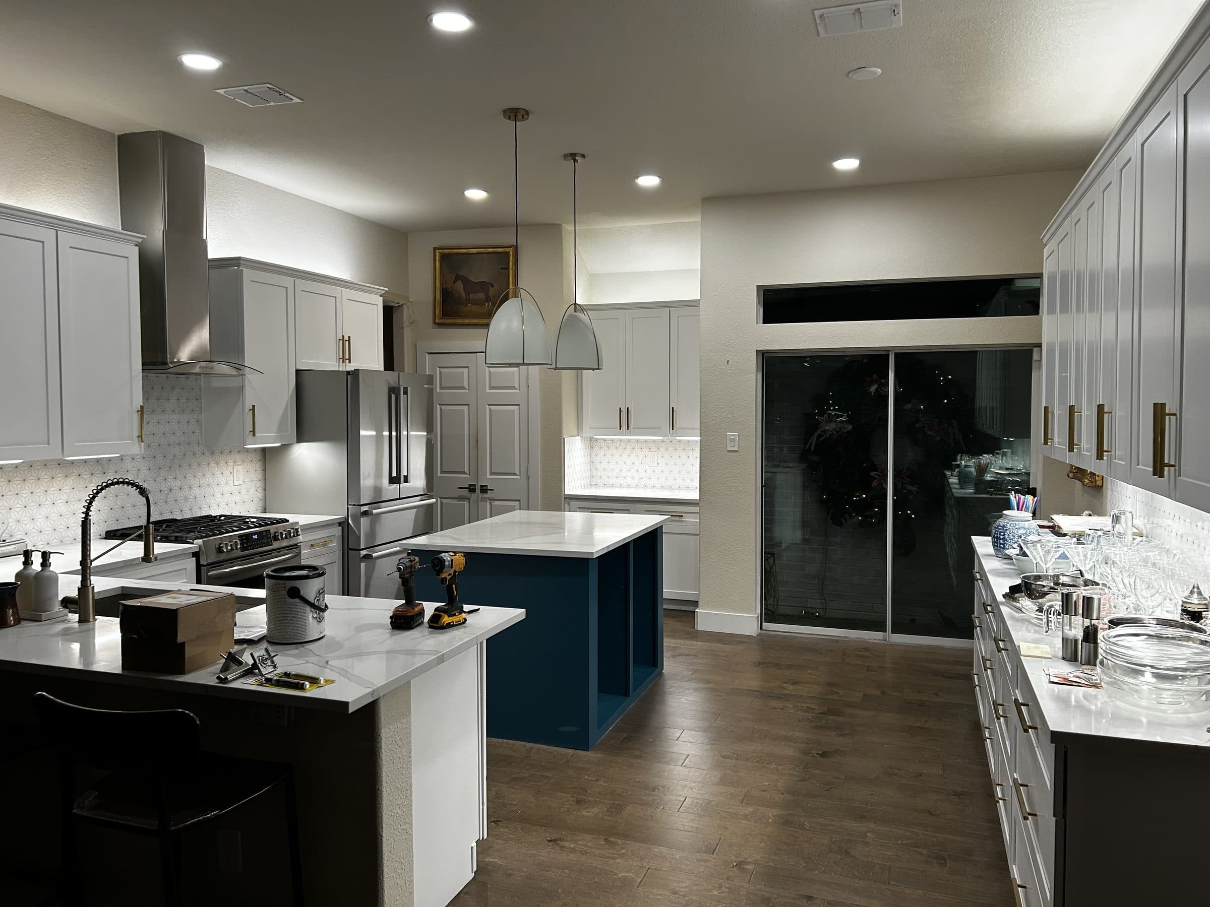 White shaker kitchen with a blue waterfall-edge quartz island, brass hardware, and a geometric tile backsplash, remodeled by HN Construction & Remodeling in Austin, TX