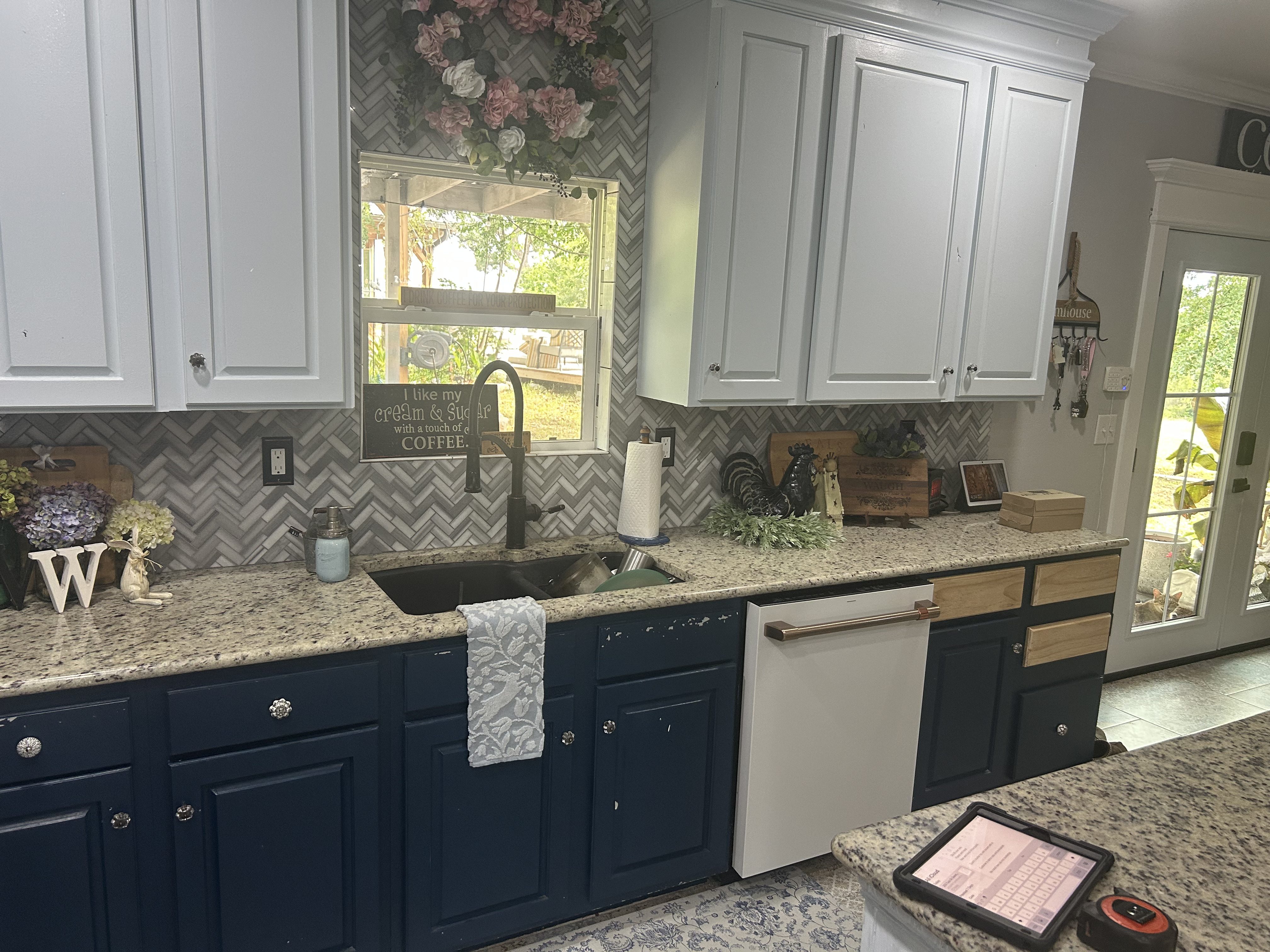 Two-tone farmhouse kitchen remodel with navy lower cabinets, white uppers, granite countertops, and a gray herringbone tile backsplash